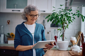 Happy senior woman using digital tablet in the kitchen.