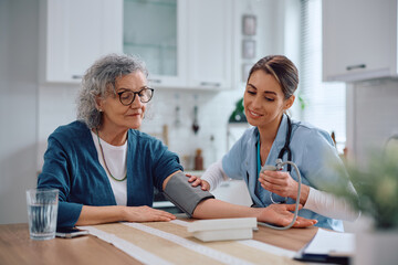 Visiting nurse checking blood pressure of senior woman at home.
