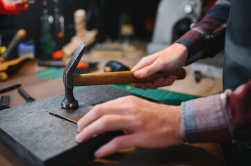 Production process. Young focused experienced master craftsman makes leather goods at his workplace