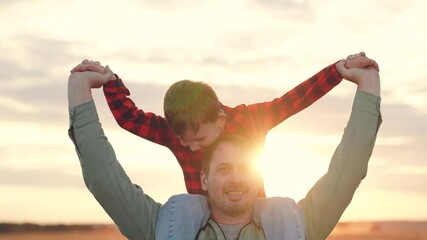 Happy father carries son on shoulders at back sunset light. Dad and boy take leisurely walk in midst of nature spending time together on sunny day. Father with young boy shares happiness