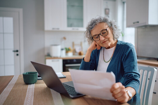 Mature woman analyzing her bills while using computer at home.