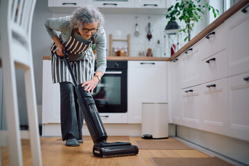 Mature woman using vacuum cleaner in the kitchen.
