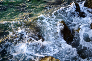 White and sparkling sea foam on top of rocks on the seashore
