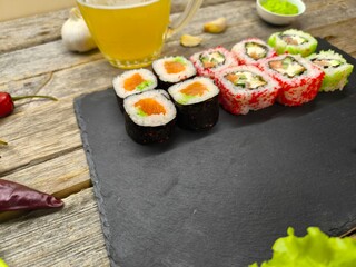 sushi on a granite board on the background of a wooden table, next to a glass of beer