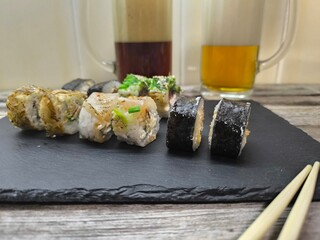An assortment of typical Japanese dishes - sushi, on a granite board with various sauces. Glasses of light and dark beer stand nearby