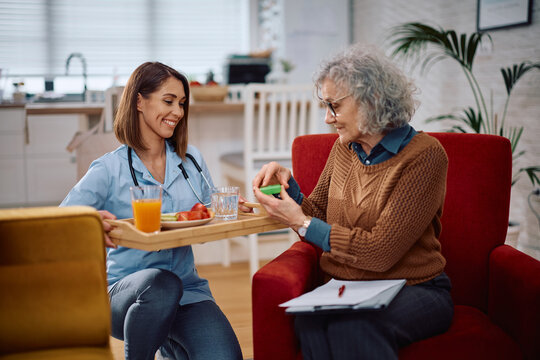 Happy nurse bringing food and medicine to senior woman during home visit.