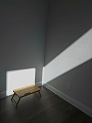 Sunlight gently streams through the window, casting a warm glow on the wooden table, while the rest of the room lingers in quiet darkness —  capturing a sense of stillness and solitude.