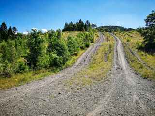 Dirt road leading up a hill in Chrobacza Łąka, Beskid Żywiecki, Poland. A rugged mountain trail surrounded by lush greenery under a bright blue sky, perfect for hiking and off-road adventures