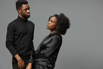 Portrait of a stylish Black couple expressing complex emotions, dressed in modern black attire...