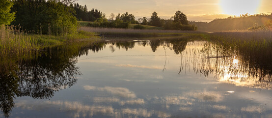 A calm lake with a sun reflecting on the water