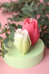 Beautiful flower shaped candles and leaves on pink background, closeup