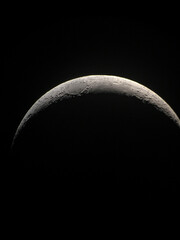 Photograph of a crescent moon highlighted against a black sky, showcasing its rugged terrain and...