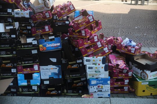 Discarded colorful cardboard fruit boxes stacked on a sidewalk, highlighting waste and recycling issues
