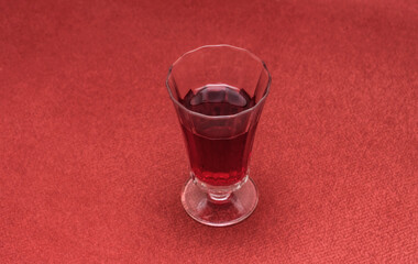 Elegant glass of red wine on red fabric background. The transparent glass showcases the vibrant hue of the beverage, creating a visually striking contrast. Selective focus.