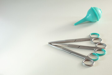 Surgical scissors and a syringe (enema bulb) lie on a white table. Medical background with free space. Photo in minimalism style.