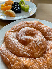Ensaimada, traditional sweet pastry of the island of Mallorca, selective focus with a plate of fresh fruit in the background.