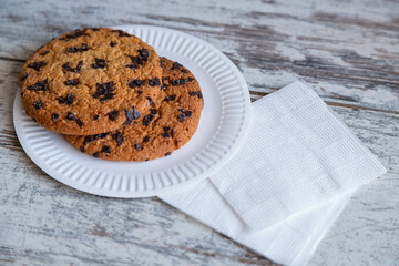 Golden-brown homemade cookies with melting chocolate chunks – a taste of childhood and homey comfort. Large cookie with chocolate chips on a plate next to napkins.