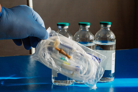 A packaged intravenous infusion system in a doctor's hands – sterility and readiness for use. Saline solution for injections in a glass bottle – an important component of medical assistance.