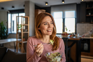 Happy woman eating fresh salad at home in modern kitchen