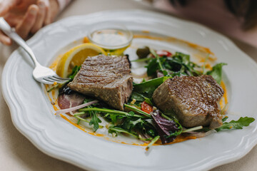 A perfectly seared tuna steak on a white plate, with green salad and a glossy drizzle of sauce.