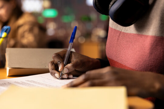 Black university scholar completing a detailed course project using educational resources and materials from the college library general database. Girl working hard on her academic notes. Close up.