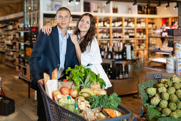 Portrait of a positive happy young couple with products in a cart, who came to the supermarket for shopping