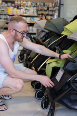 Man choosing a baby troller in a children shop. Man looking prices for baby trollers in a shop.