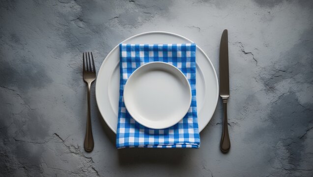 Empty white plate with blue napkin on a gray stone surface.
