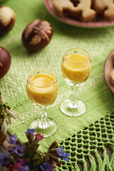 Two glass cups of Eiecognac with Easter eggs and spring flowers on green tablecloth