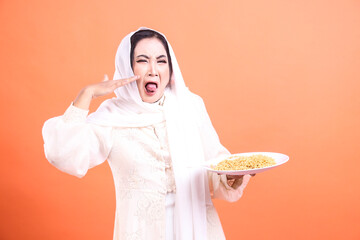 Muslim woman in traditional dress expressing disgust and aversion to noodles held on a plate in her...
