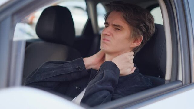 A tired driver stretches his neck from an uncomfortable seat behind the wheel