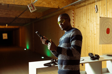 Man wearing protective goggles reloading gun with bullets in shooting range, following safety protocols. Person loading pistol, carefully handling weapon following methodical safety rules