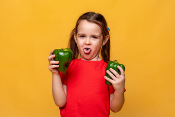 Cute little girl in a red t-shirt on a yellow background, holding two green peppers in her hands...