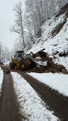 A heavy-duty loader clears a snow-covered mountain road, pushing through thick mud and ice