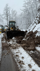 A heavy-duty loader clears snow and soil from a winding mountain road