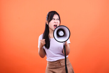 Woman shouting into a megaphone with a determined expression isolated on an orange background