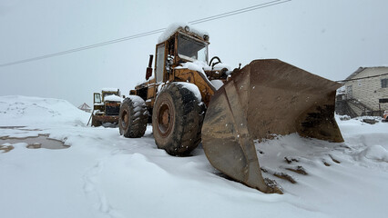 A rugged bulldozer, dusted with fresh snow, stands still in the winter storm