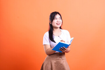 Young woman writing in a blue notebook with pen, with an orange background for education or work concept