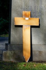 an unmarked wooden cross leans on the back of a gravestone in a cemetery