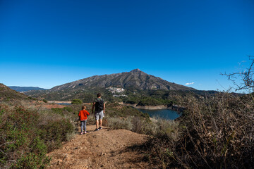 Fototapeta premium Father and son hiking with scenic mountain view and clear blue sky, La Concepcion reservoir in Marbella