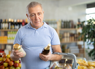 Concerned old man is deciding between kinds of beer in the supermarket