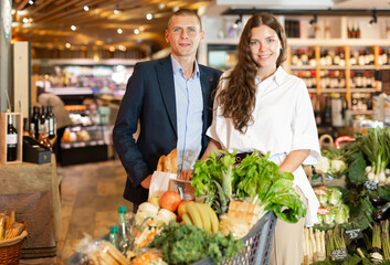 Portrait of young woman and man with shopping cart at vegetables department at supermarket