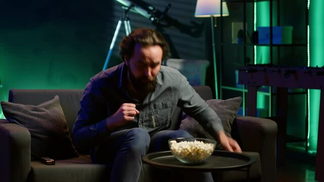 Man in apartment chocking on food while watching movie on TV and eating popcorn. Person getting throat clogged while swallowing snack, doing heimlich maneuver on couch, fighting for his life, camera A