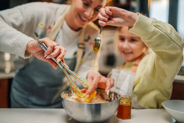 Mother and daughter adding honey while whisking ingredients in bowl