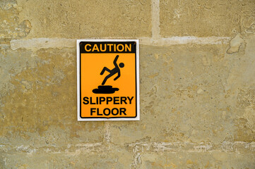 Caution Slippery Floor yellow sign with black letters stone wall background no people copy space.