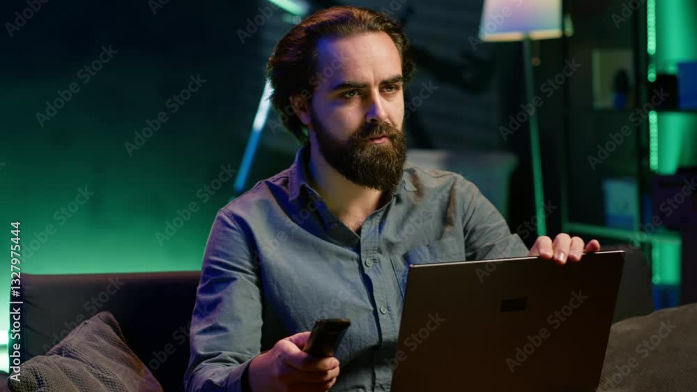Poster man watching shocking breaking news story on tv while using laptop in neon lit apartment. person tur