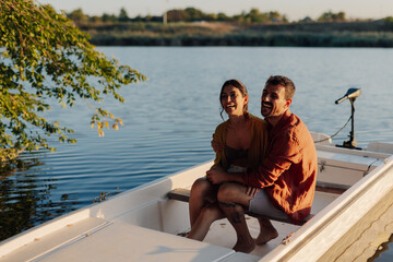 Happy couple laughing and enjoying a romantic boat ride on a lake at sunset