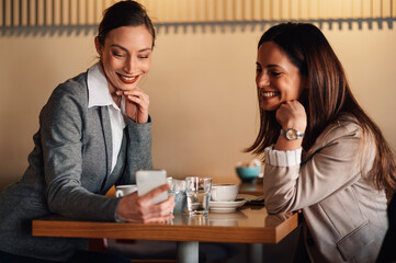 Businesswomen looking at smartphone and smiling during coffee break