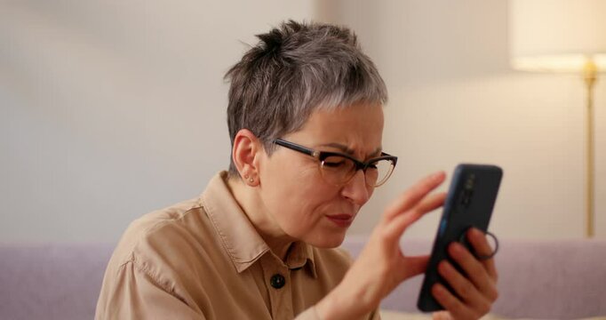 Senior woman with poor eyesight holds smartphone close to face