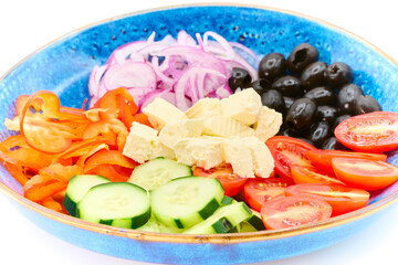 Greek salad with Cherry tomatoes, cucumber, peppers, olives, Greek feta cheese, red onions in the blue plate with white background